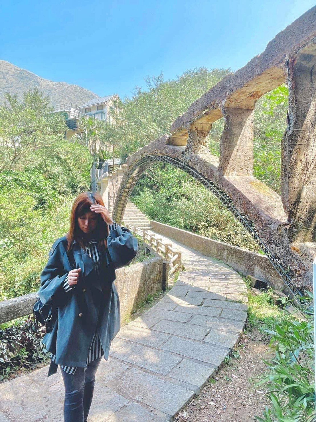 女生走在山徑石階步道上,旁邊是石造舊拱橋與山景